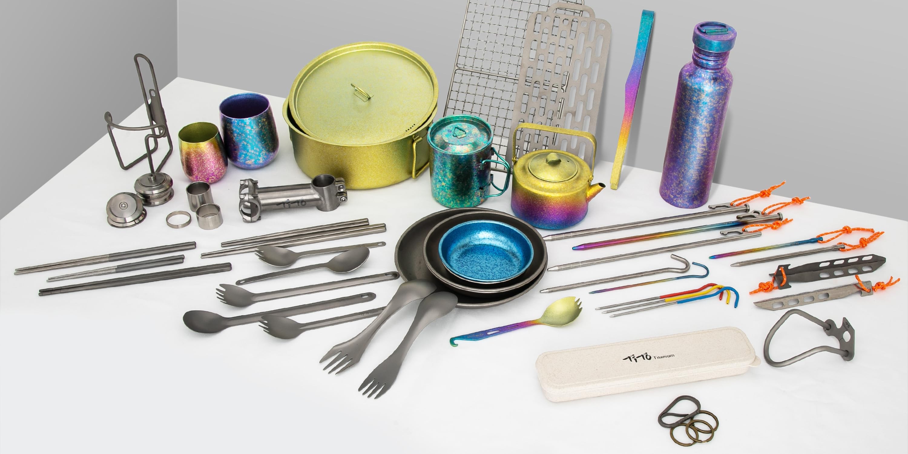 Titanium camping gear flat lay — pots, cups, cutlery, grills and EDC
